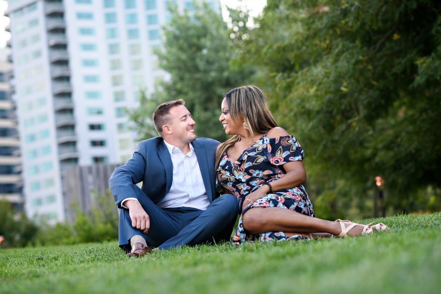 An engaged couple sit in the grass along the Hudson in Hoboken for their engagement session.